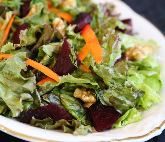 closeup of green salad with beets and walnuts in a white dish