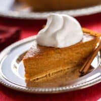 Vegan pumpkin pie with dairy free whipped cream and cinnamon sticks on holiday table