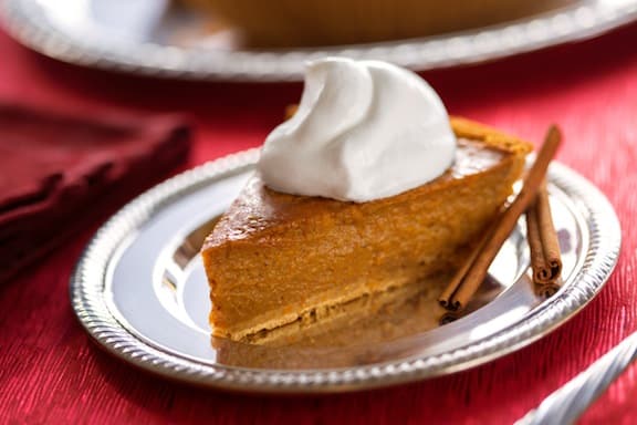 Vegan pumpkin pie with dairy free whipped cream and cinnamon sticks on holiday table