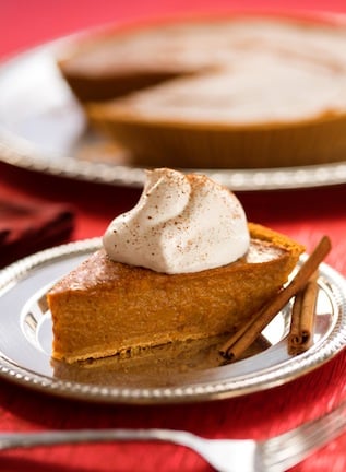 Vegan pumpkin pie with dairy free whipped cream and cinnamon sticks on holiday table