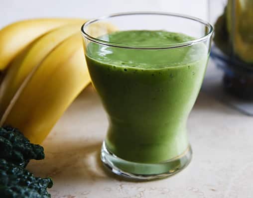 Green velvet smoothie (kale, banana, and avocado) next to bunch of bananas