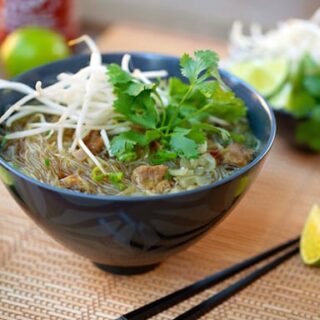 Bowl of vegan pho bo with seitan and rice noodles, served with lime wedges and chopsticks