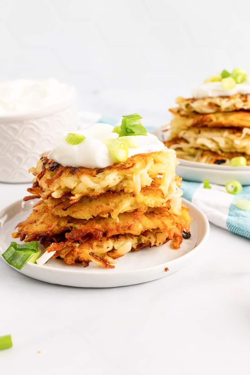 plate of stacked vegan potato pancakes topped with sour cream and green onions