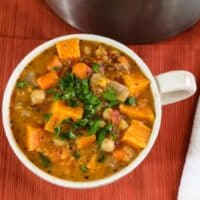 Chunky sweet potato bisque with chickpeas and fresh parsley in a white mug