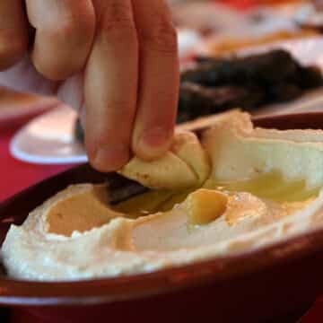 A man dipping a pita bread slice in a traditional hummus plate