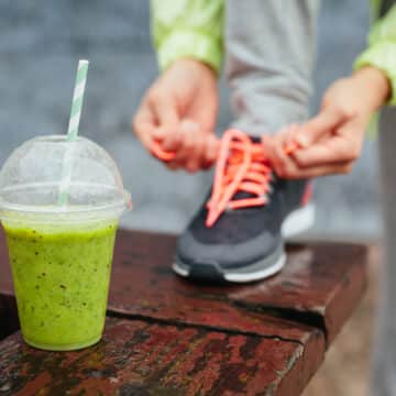 Green detox smoothie cup and woman lacing running shoes before workout on rainy day. Fitness and healthy lifestyle concept.