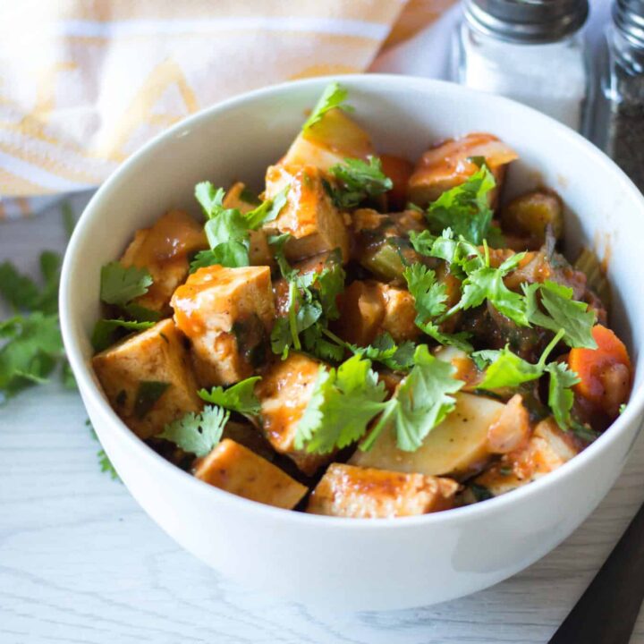 Tofu and vegetable stew served in a white bowl with fresh cilantro