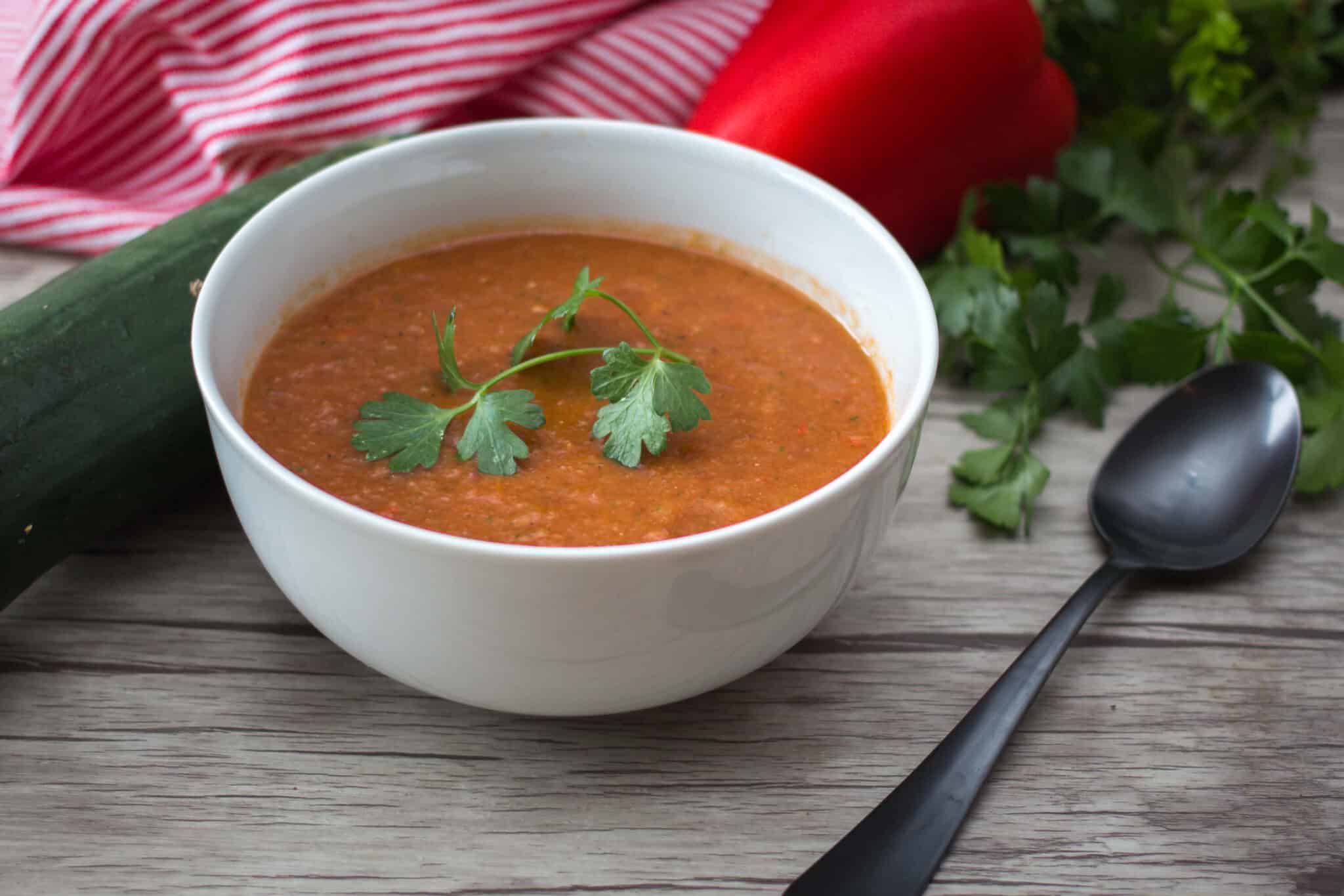 bowl of authentic gazpacho soup on a table by veggies and napkin