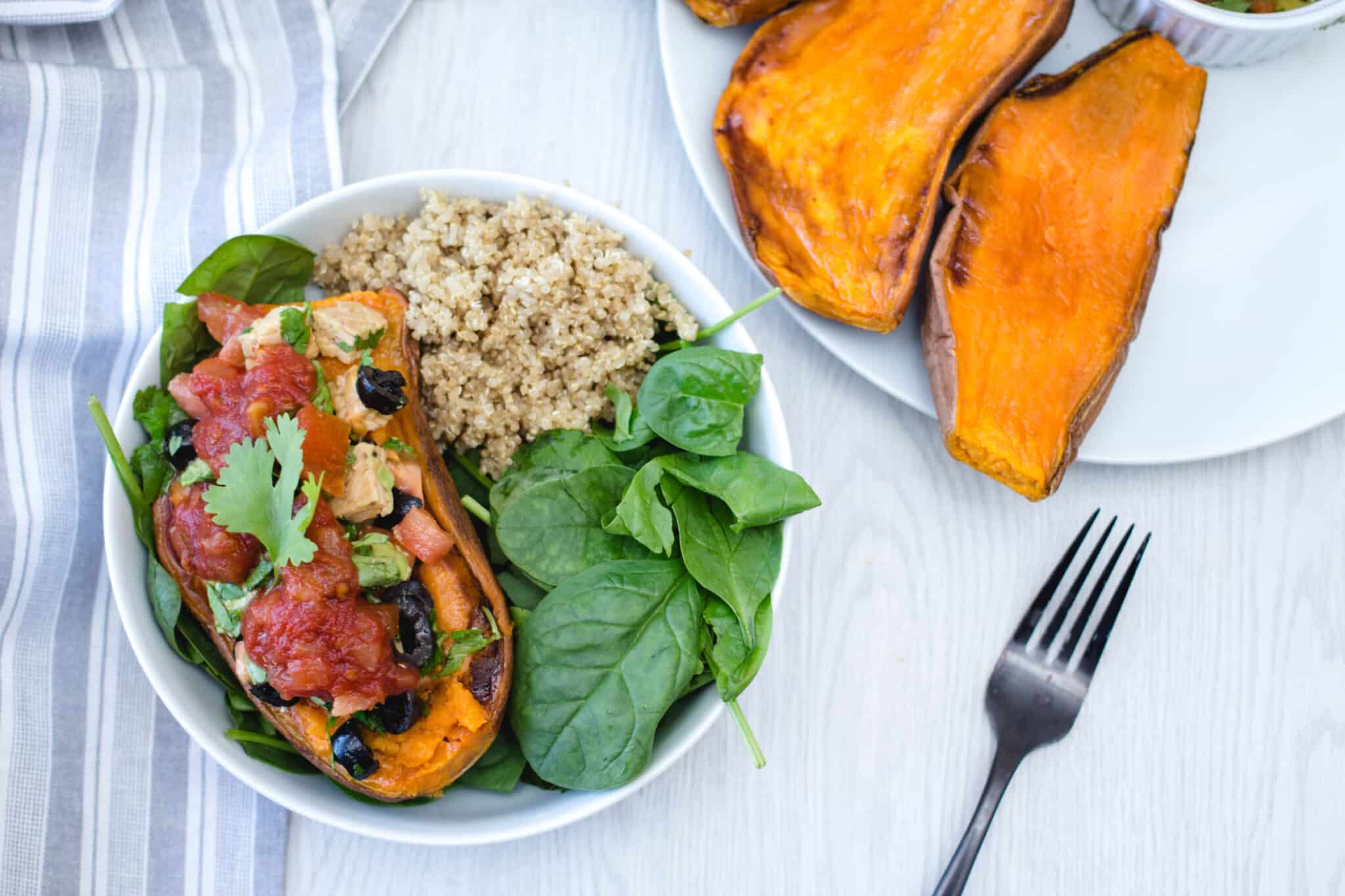 Baked sweet potato halves stuffed with black beans and salsa, served with quinoa and spinach