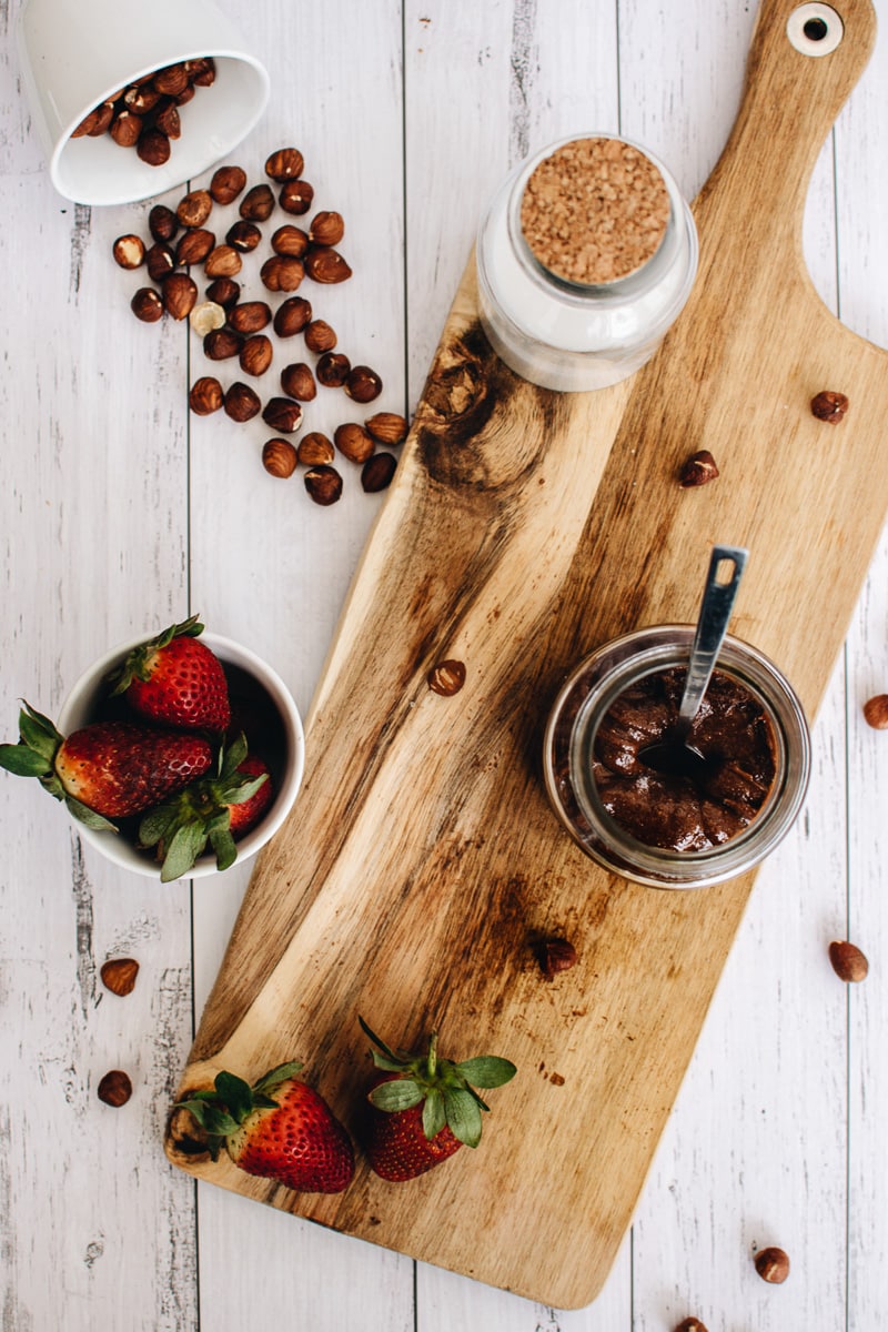 Tarro de nutella vegana casera sobre una tabla de cortar con fresas y avellanas