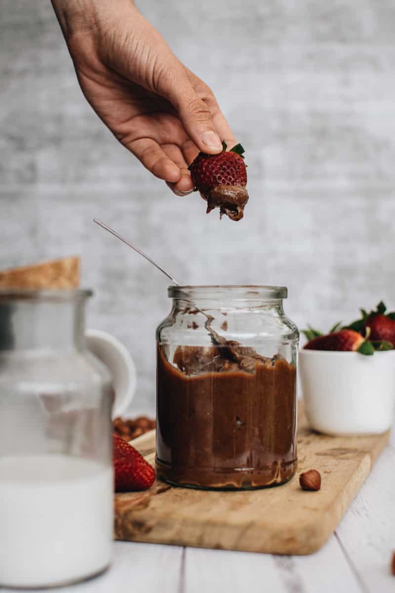 strawberry being dipped into jar of homemade vegan nutella