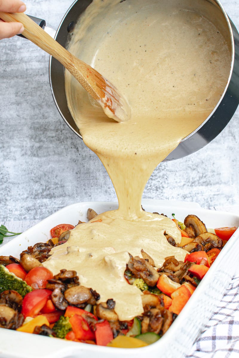 pouring vegan cheese sauce over roasted veggies