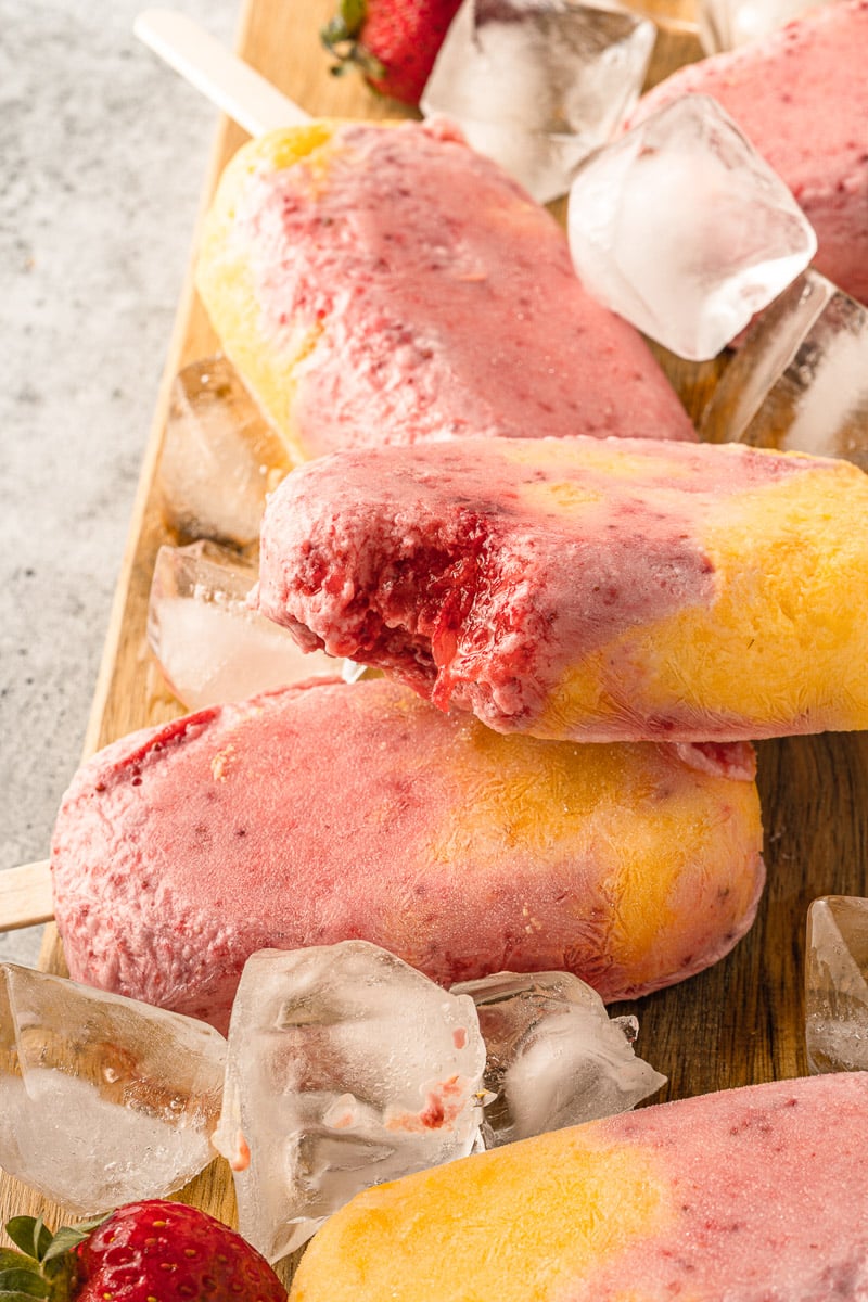 stack of vegan strawberry mango popsicles with a bite out