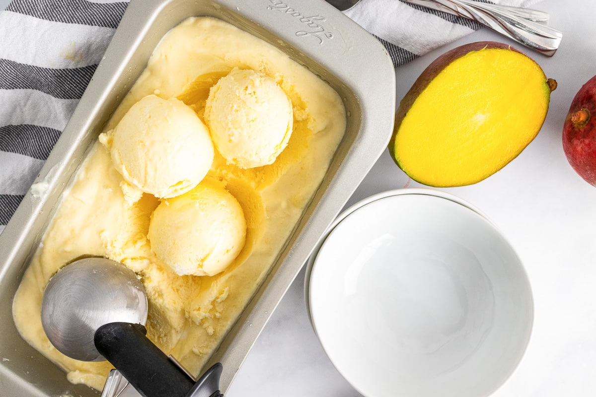 vegan mango ice cream in a loaf pan with scoops rolled out on top