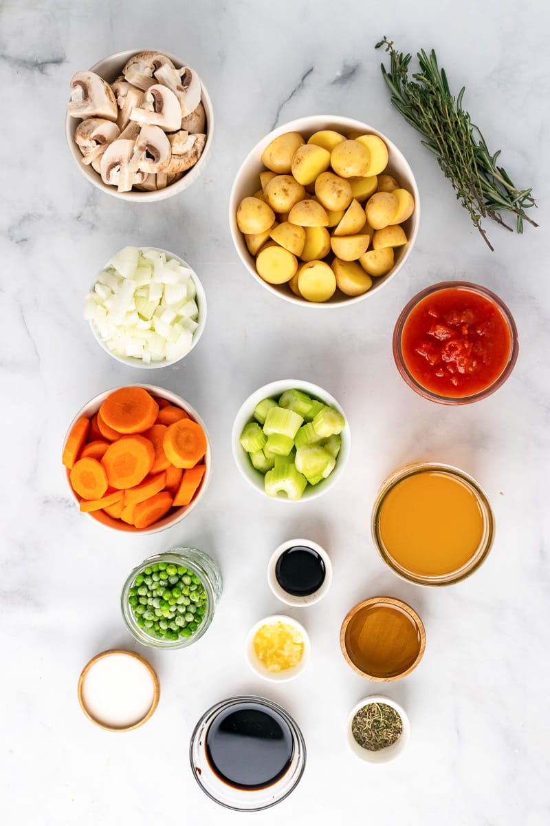 ingredients for old-fashioned vegan stew in small bowls, including potatoes, carrots, mushrooms, peas, and broth