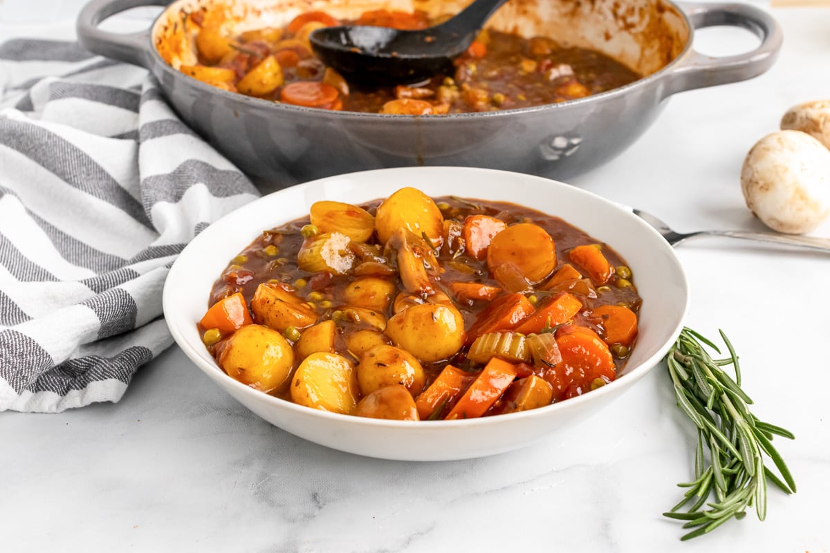 white bowl with old fashioned vegan stew in front of a gray saucepan