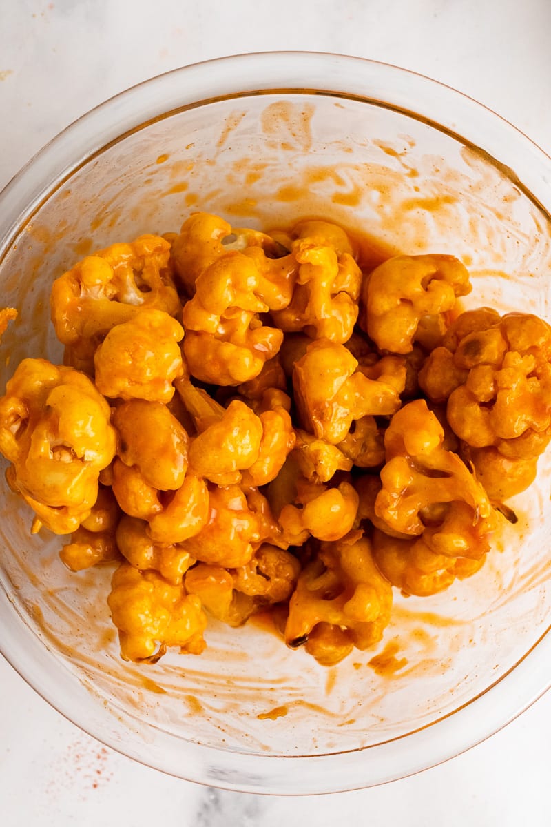 vegan buffalo cauliflower florets mixed with sauce in bowl