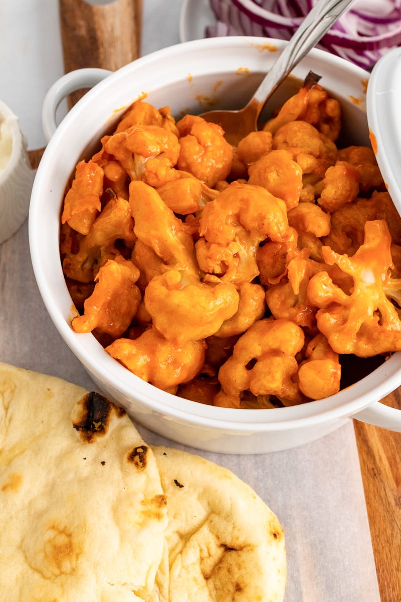 vegan buffalo cauliflower in white pot next to naan breads