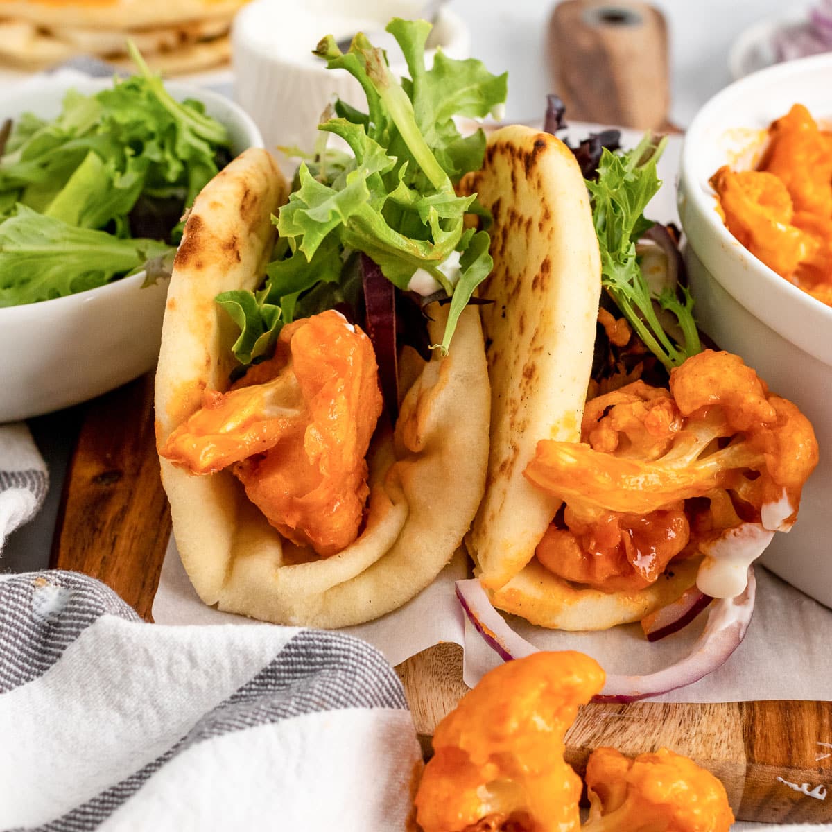 two buffalo cauliflower wraps between bowl of lettuce and bowl of buffalo cauliflower