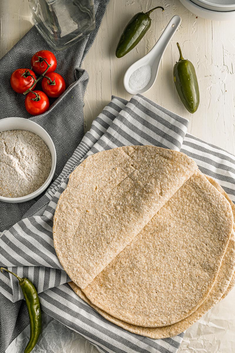 homemade flour tortillas stacked on a blue and white striped dish towel