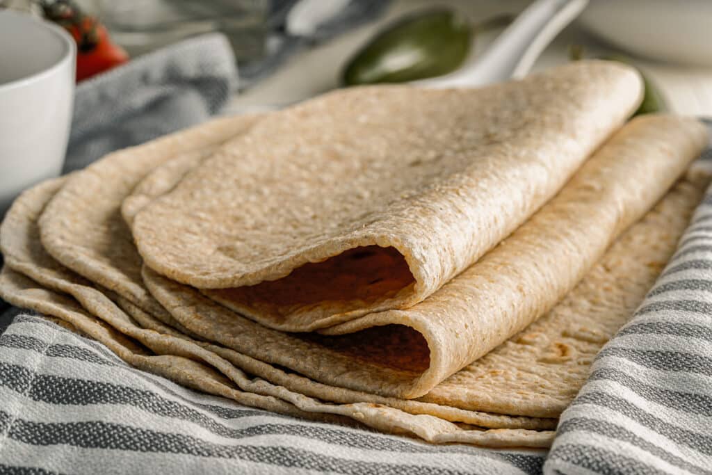 side view homemade flour tortillas stacked and folded on a dish towel