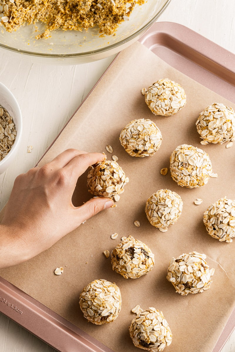 hand placing pumpkin protein balls onto baking tray