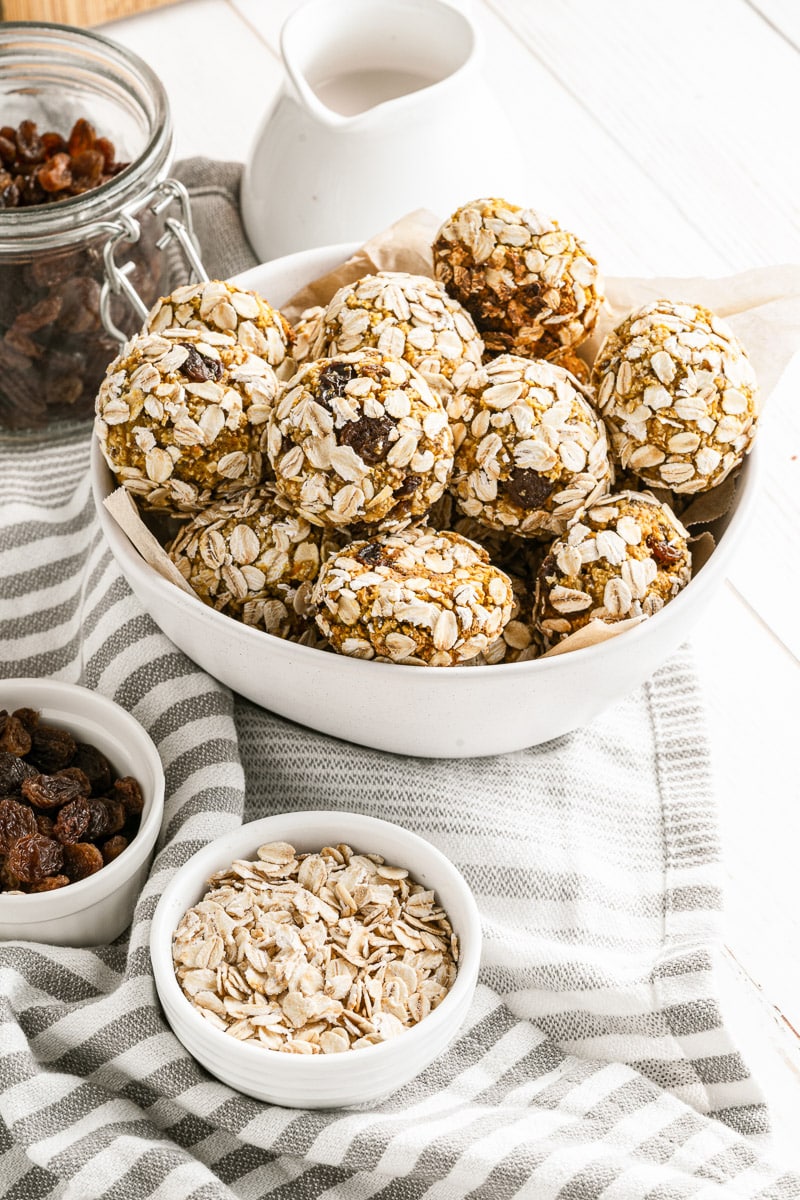 Bowl of oat-coated pumpkin protein balls with small bowls of rolled oats and raisins