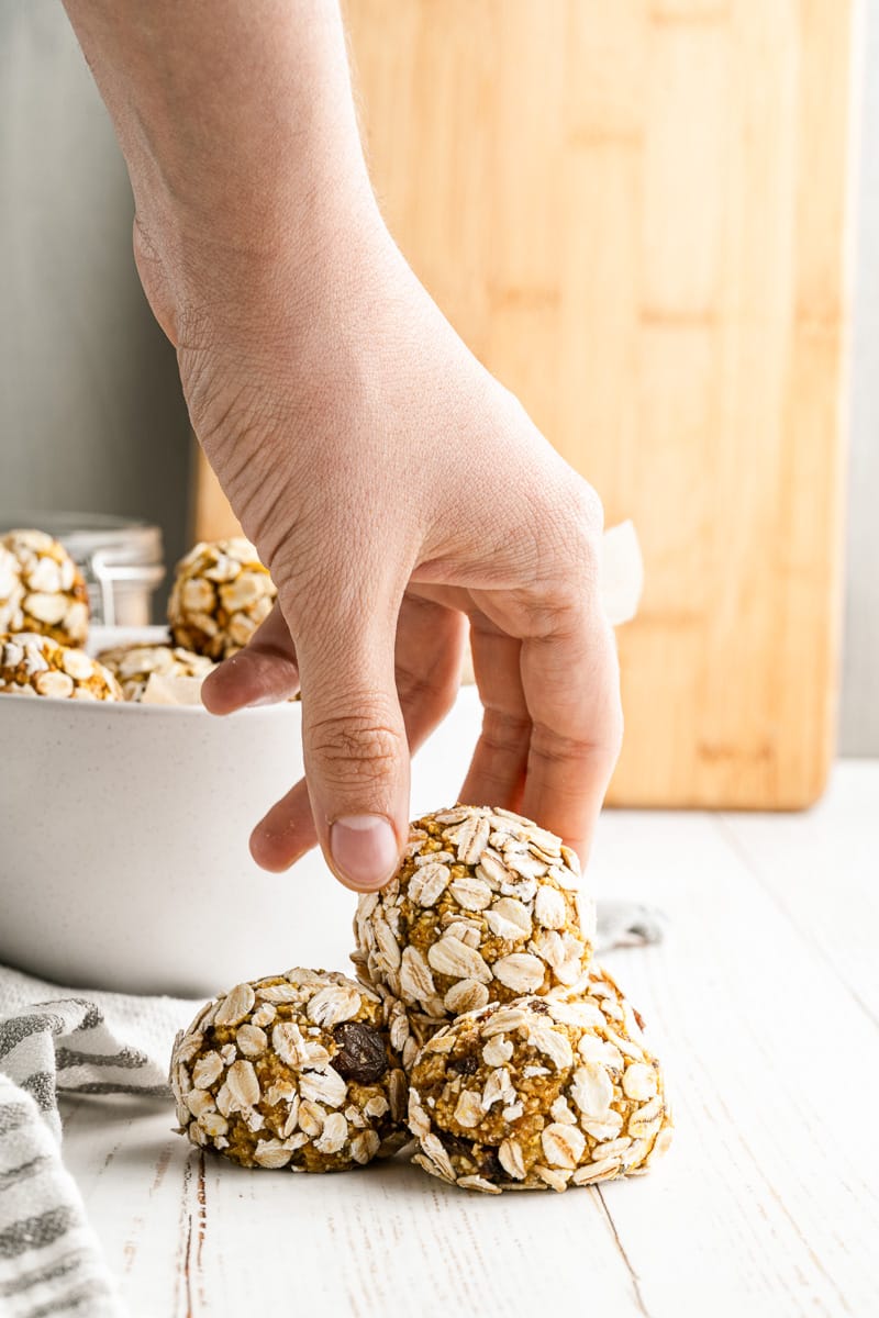 hand grabbing pumpkin protein ball from top of small pyramid stack of protein balls