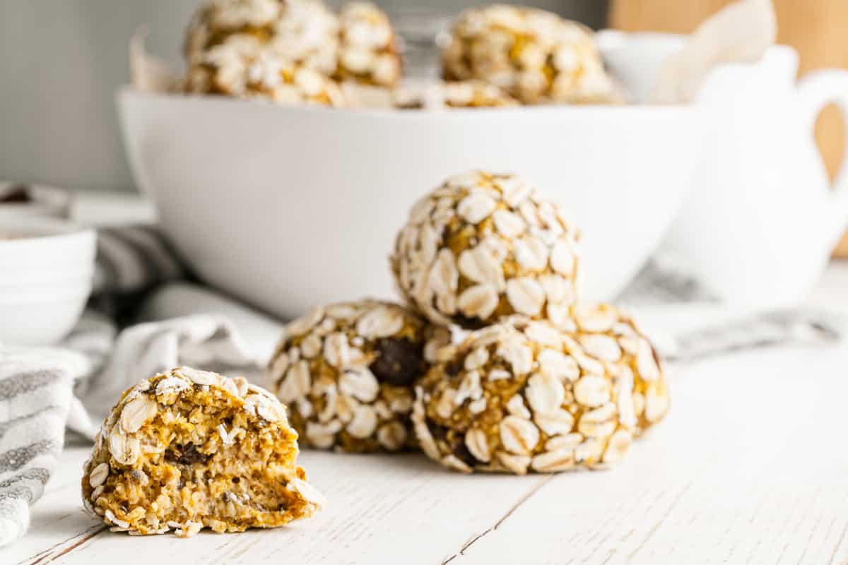 Stack of oat-coated pumpkin protein balls with one broken open to show the soft raisin-studded center