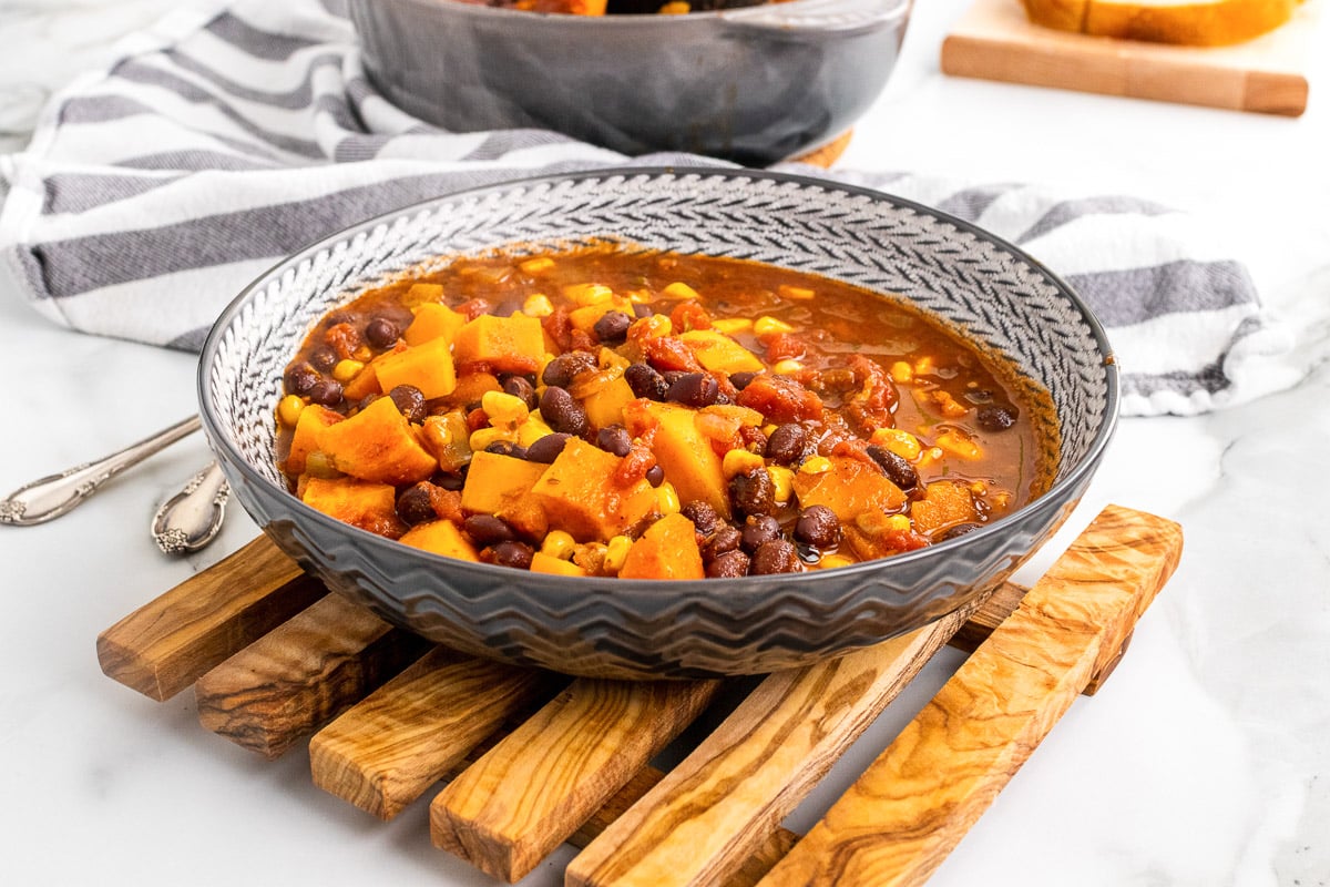 side view bowl of sweet potato black bean chili on wooden serving board