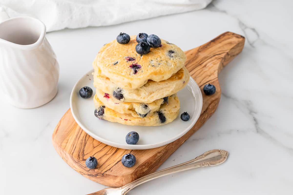 stack of vegan blueberry pancakes on white plate on top of wooden cutting board on marble countertop