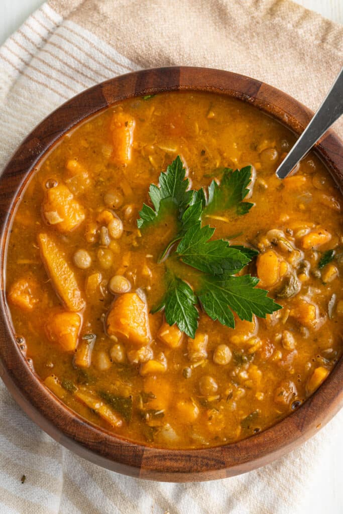 Overhead view of vegan sweet potato lentil soup in a wooden bowl with a spoon