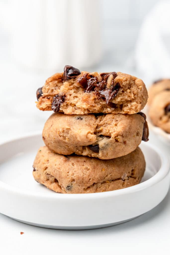 Stack of three chickpea chocolate chip cookies on a white plate, the top cookie broken open to show melted chocolate