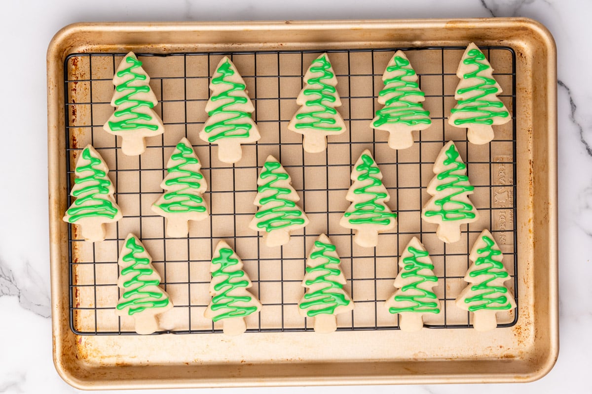 adding green frosting to the christmas tree shaped vegan christmas cookies