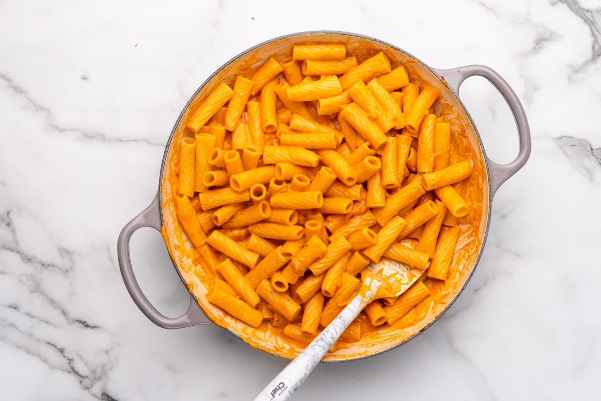 tossing the vegan vodka sauce with rigatoni pasta