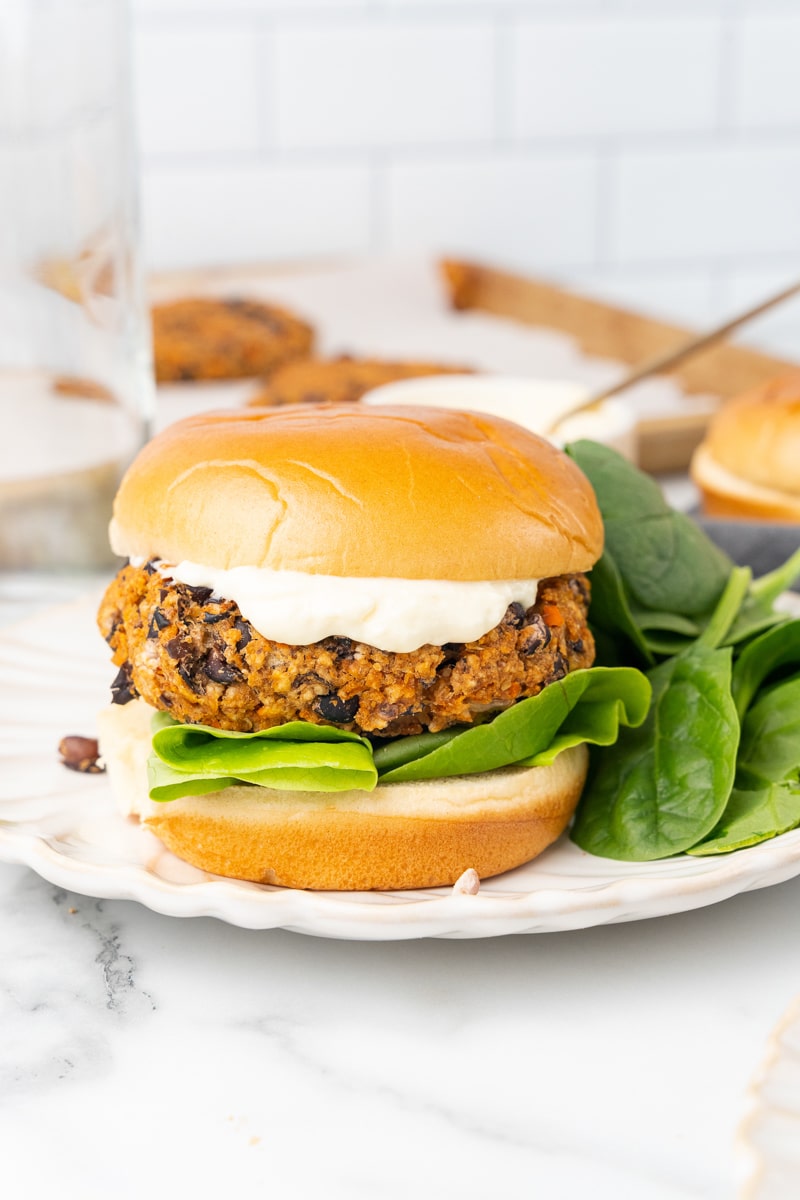 vegan burger being served on a white plate with fresh salad