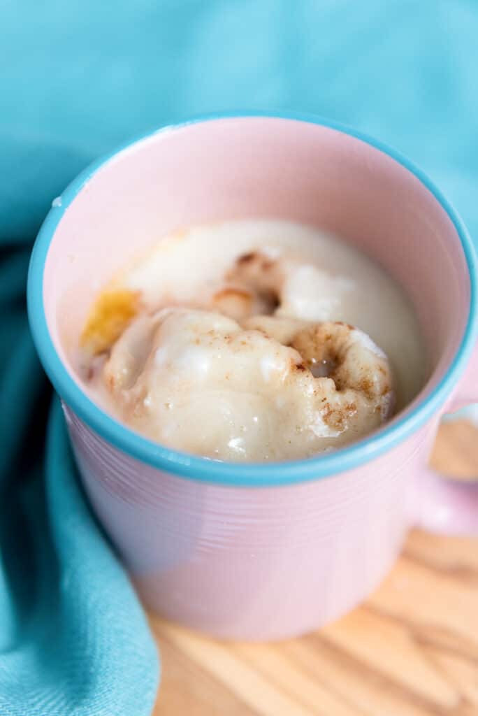 Vegan cinnamon roll topped with glaze in a pink mug