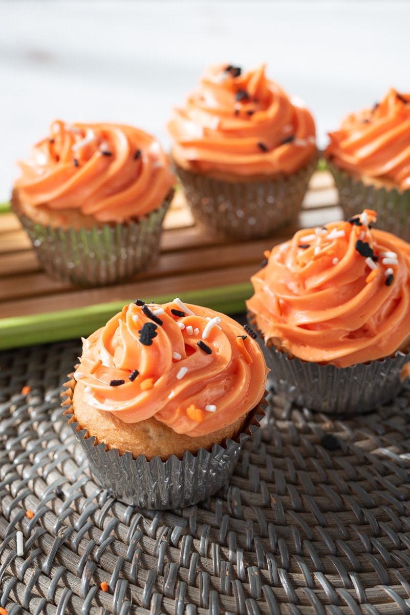 Vegan Halloween cupcakes on a woven placemat with a green tray of cupcakes behind them