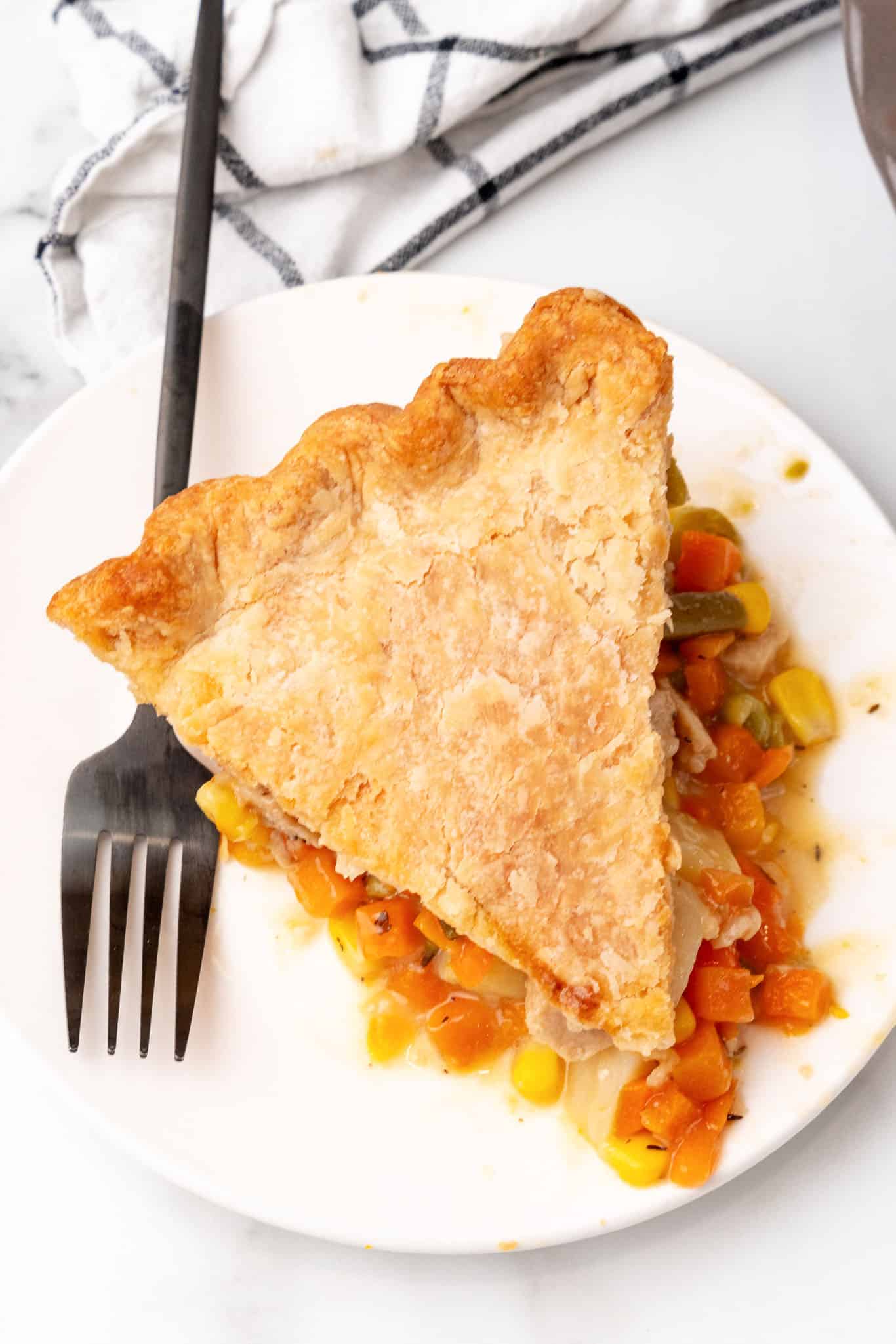 Slice of vegan pot pie on a white plate with a black fork