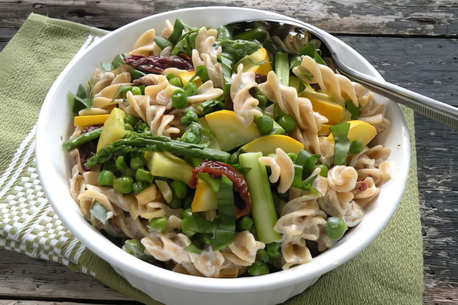 Vegan pasta alfredo with asparagus, peas, yellow squash, and sun-dried tomatoes