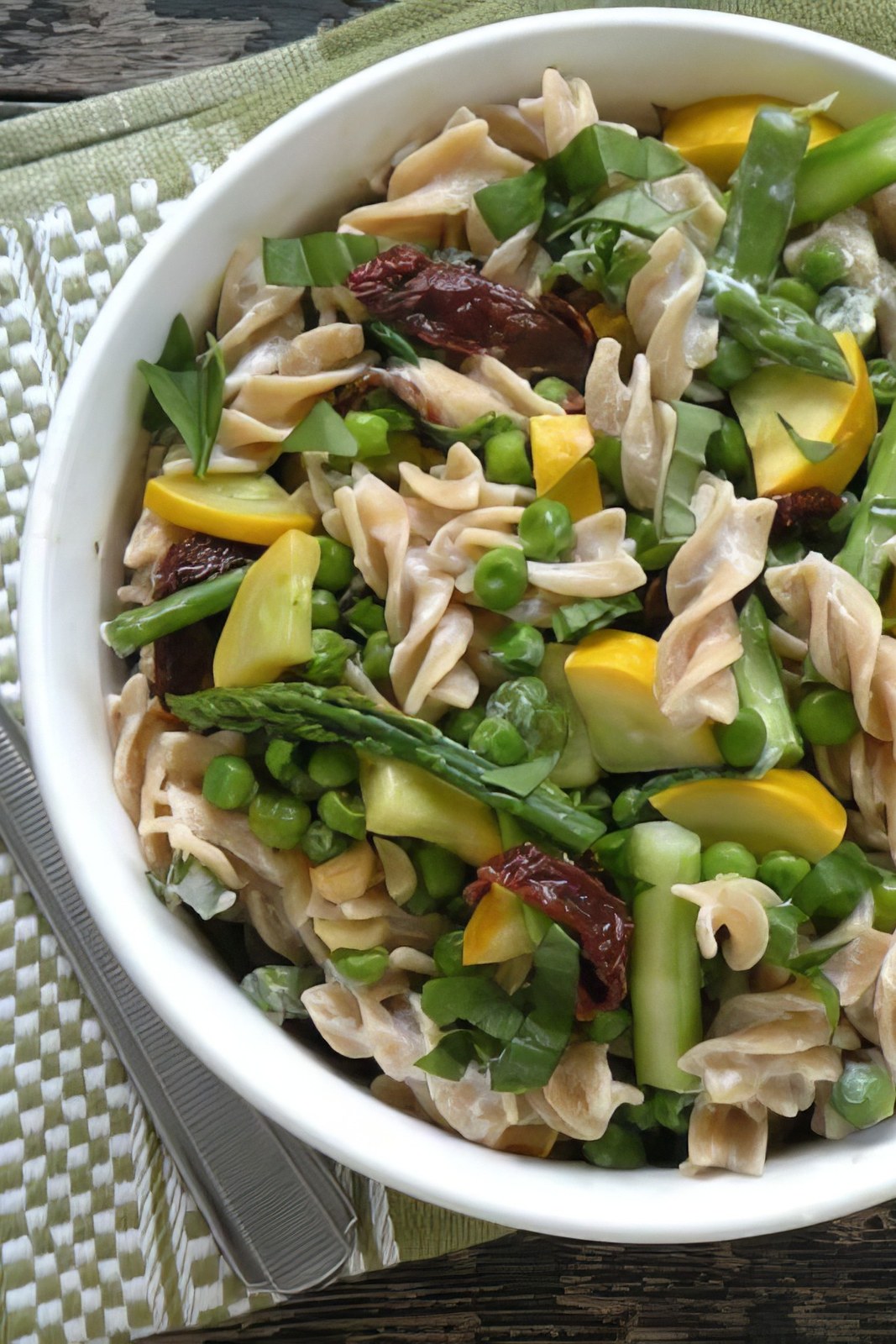 Bowl of vegan pasta alfredo with spring vegetables and sun-dried tomatoes