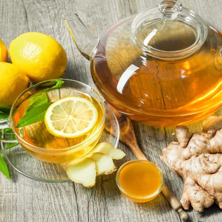A glass teapot and cup of lemon ginger tea with fresh lemon slices, ginger root, and honey