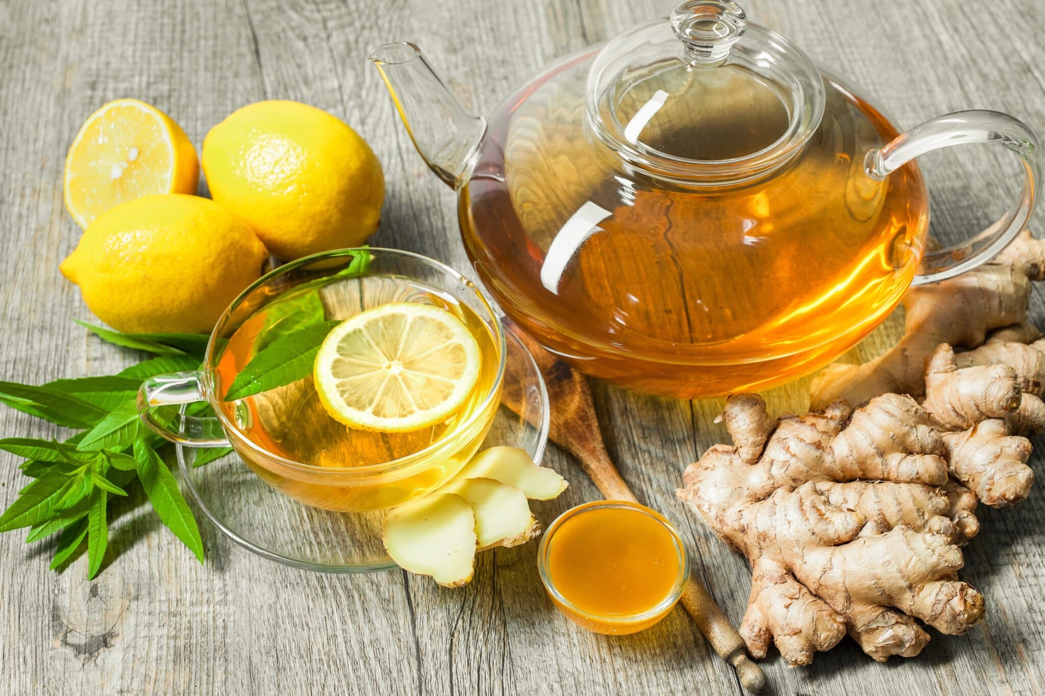 A glass teapot and cup of lemon ginger tea with fresh lemon slices, ginger root, and honey