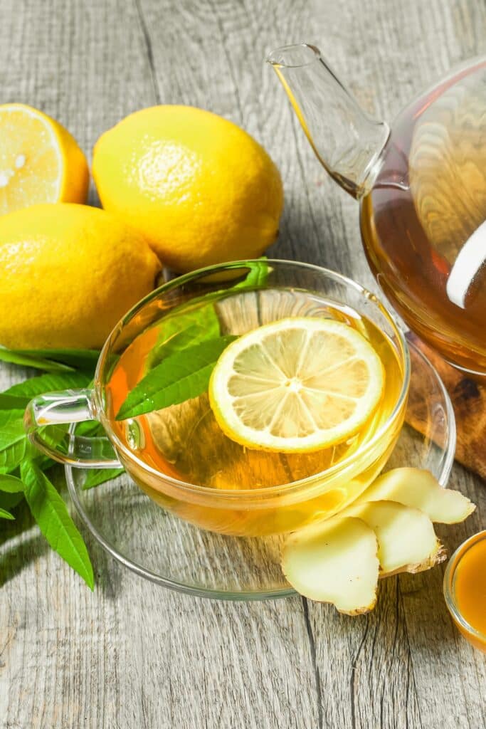 Overhead view of a cup of lemon ginger tea with lemon verbena, fresh ginger slices, and honey