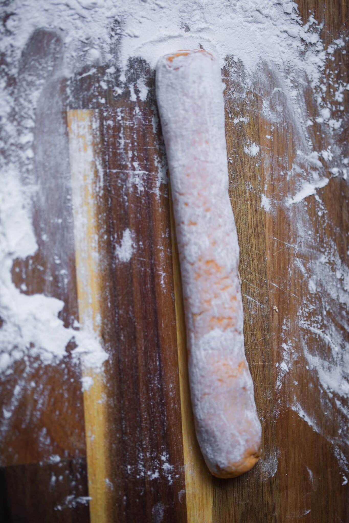 Rope of sweet potato gnocchi dough on a floured wooden board