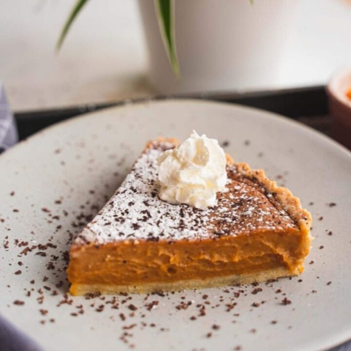 Slice of vegan pumpkin pie topped with whipped cream on a white plate