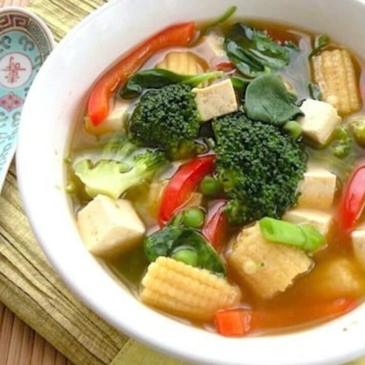 Asian tofu vegetable soup with broccoli, baby corn, red pepper and tofu cubes in a white bowl