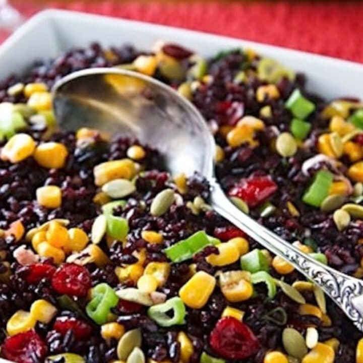 Black rice with corn, cranberries, scallions, and pumpkin seeds in a white serving dish with a silver spoon