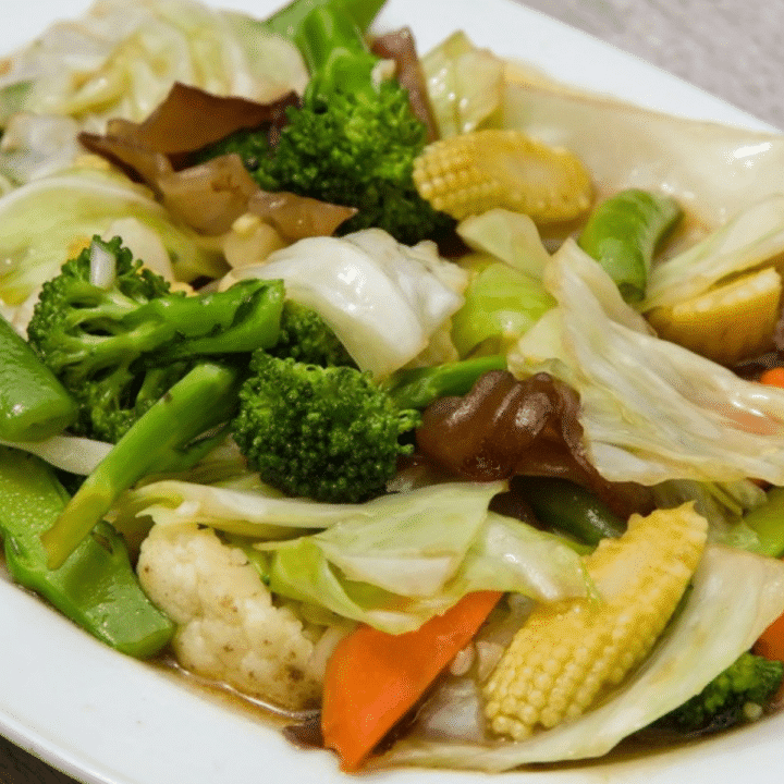 Chinese vegetable stir fry (Buddha's Delight) with broccoli, cabbage, baby corn and snap peas on a white plate