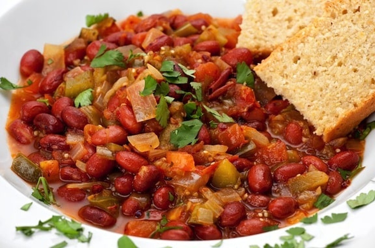 Bowl of vegan chili with beans and fresh cilantro served alongside slices of cornbread
